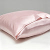 A light pink satin pillowcase on a white surface with a neutral gray background.