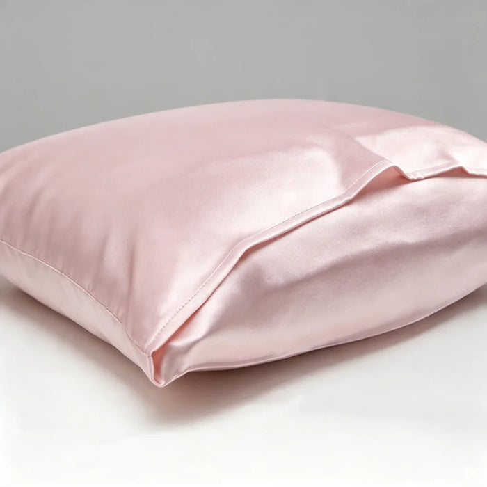 A light pink satin pillowcase on a white surface with a neutral gray background.