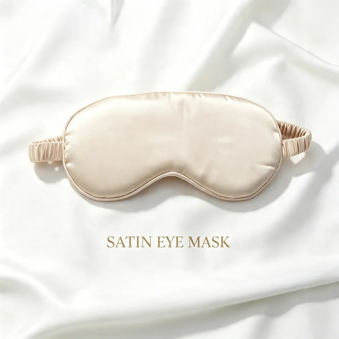 A satin sleep mask in a soft champagne beige color, laid flat on a draped white satin fabric background with the text 'SATIN EYE MASK' printed below it.