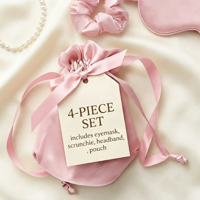 A pink satin 4-piece set gift pouch with a drawstring and ribbon, attached to a paper tag that reads '4-PIECE SET includes eyemask, scrunchie, headband, pouch.' Styled on a cream satin background with partial views of a pink eye mask, pink scrunchie, pearl necklace, and a pink headband.