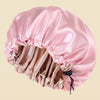 A pink satin hair cap with a drawstring closure, shown against a solid light beige background.