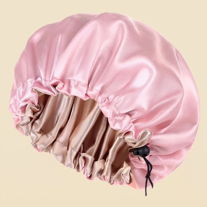 A pink satin hair cap with a drawstring closure, shown against a solid light beige background.