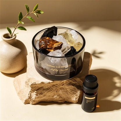The ZenPulse Luminous Crystal Diffuser British Pear Freesia variant, featuring a mix of raw Tiger's Eye, Citrine, and clear crystals in a dark glass bowl. The set is beautifully arranged on a rustic stone base next to a minimalist ceramic vase and an essential oil bottle, captured in warm, directional sunlight.