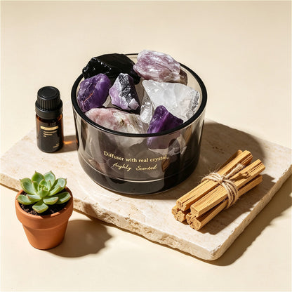 The ZenPulse Luminous Crystal Diffuser Lavender variant, featuring a dark glass bowl filled with raw Amethyst and clear quartz crystals. The set is displayed on a stone slab next to a small succulent, a bottle of essential oil, and a bundle of Palo Santo sticks, creating a serene wellness atmosphere.
