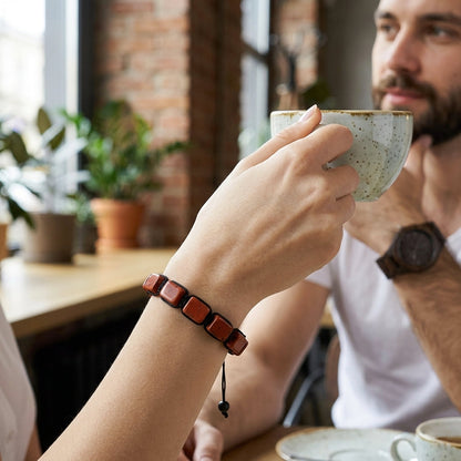 A lifestyle photo of a person wearing the ZenPulse Earth Anchor bracelet, featuring polished Red Jasper gemstone pillars. The person is holding a coffee cup in a cafe setting, showcasing the bracelet's versatile and modern look for daily wear.