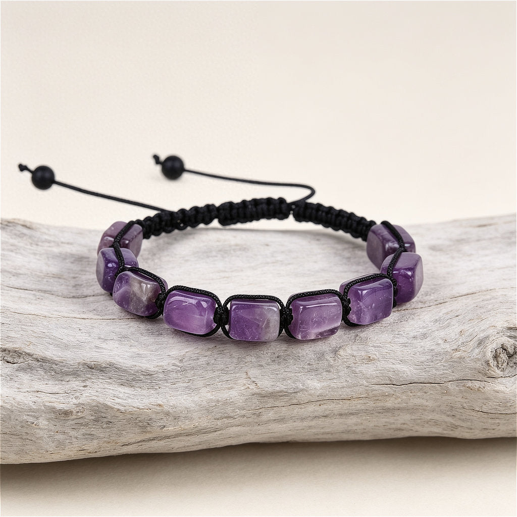 A hand-woven adjustable bracelet featuring polished rectangular purple amethyst gemstone pillars, from the ZenPulse Element Collection, model Deep Serenity. The bracelet is displayed on a rustic light wood branch against a soft beige background.