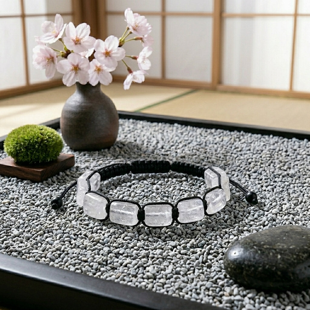 A hand-woven adjustable bracelet featuring polished rectangular White Crystal gemstone pillars from the ZenPulse Element Collection. The Pure Clarity model is elegantly placed on a bed of fine grey pebbles in a Japanese-inspired Zen garden setting, with a cherry blossom vase and shoji screen background, showcasing the icy transparency of the stones.